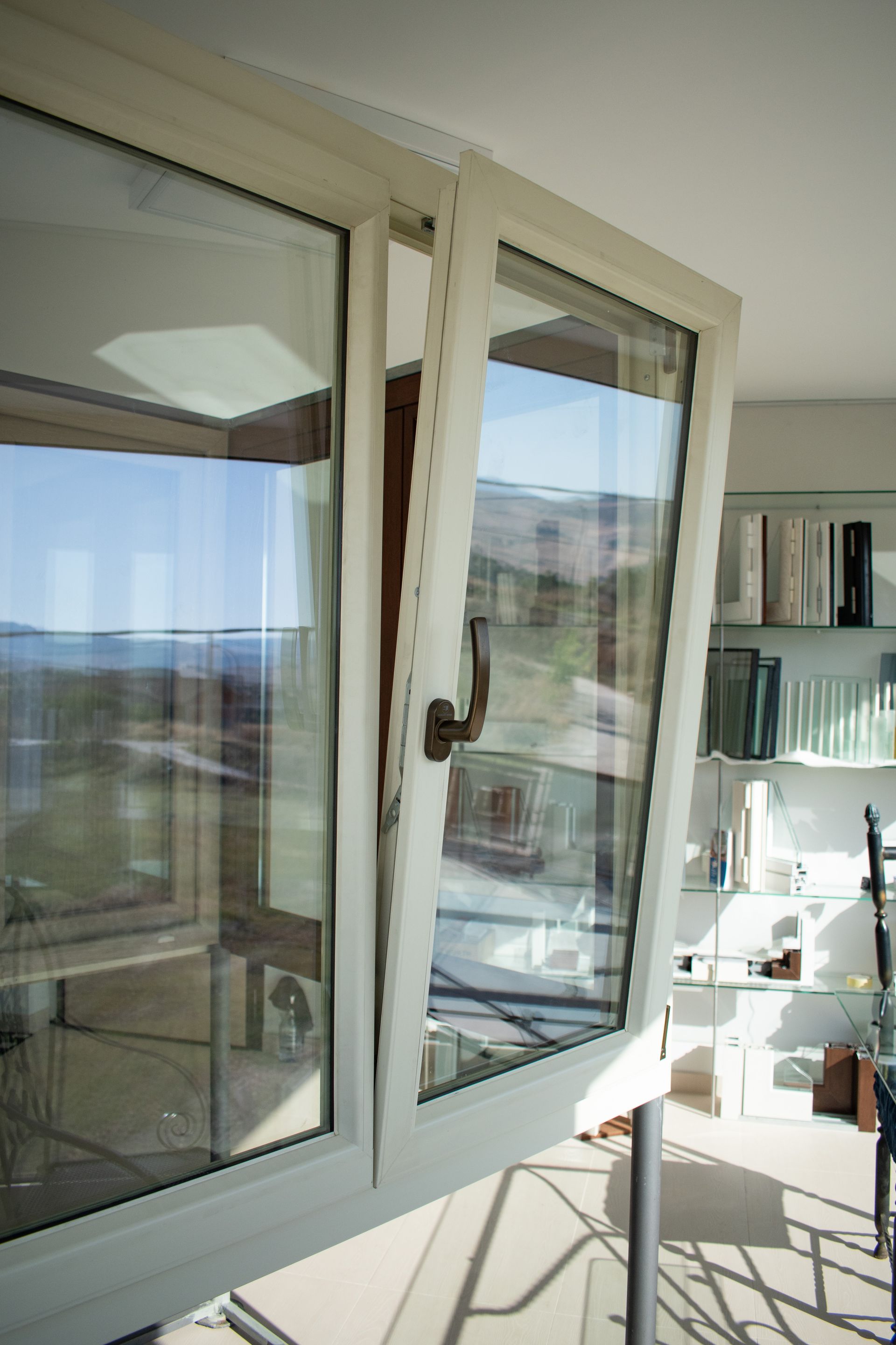 In una stanza interna, una finestra a vasistas color crema è aperta verso l'interno, con una libreria sullo sfondo.