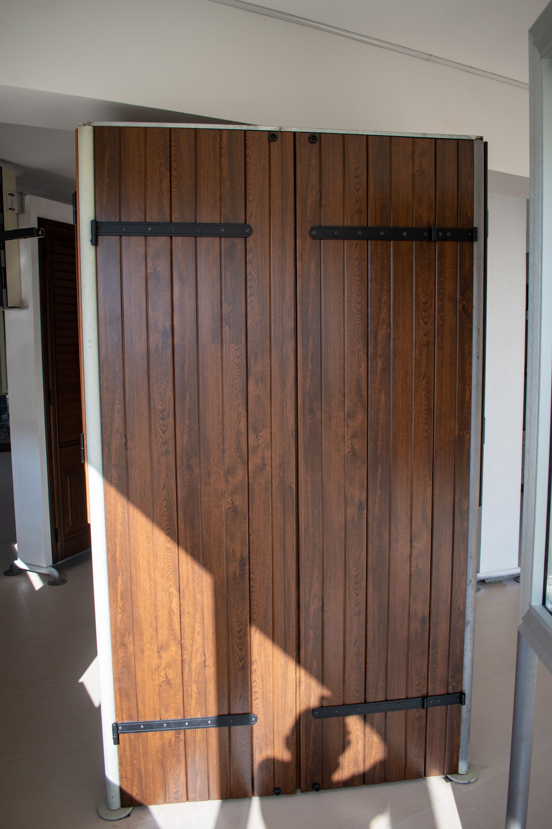 Due persiane verticali in legno con cerniere scure, esposte in posizione verticale su un pavimento chiaro in un ambiente interno.