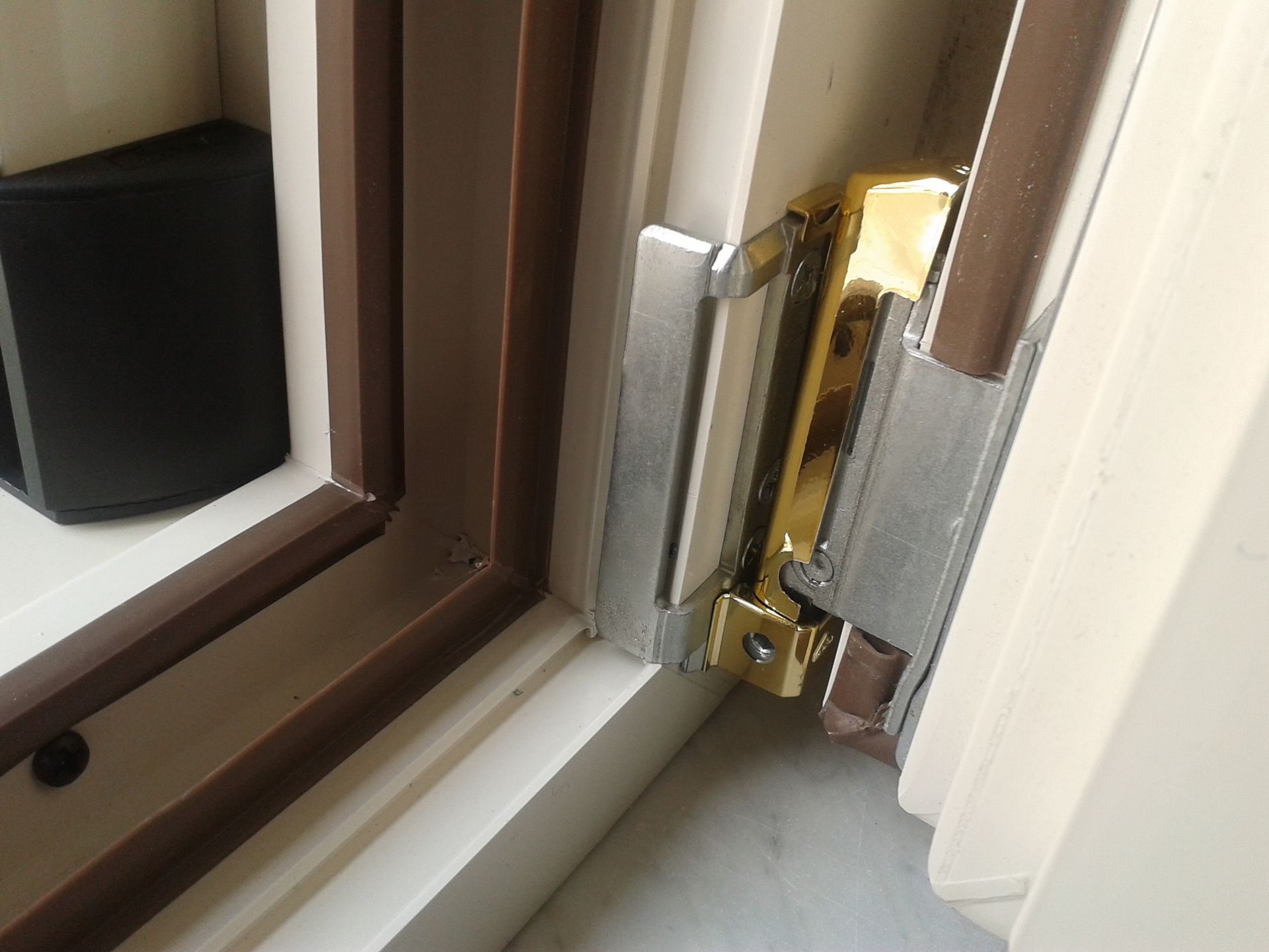 Un meccanismo di chiusura o bloccaggio per finestra in metallo argentato, fissato a un telaio di finestra bianco con finiture marroni.