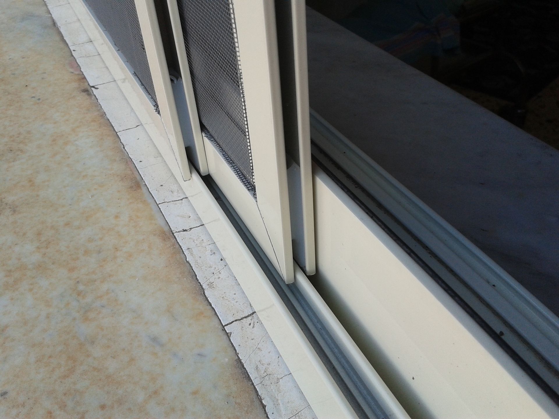 Una vista ravvicinata di porte scorrevoli in vetro e pannelli beige che scorrono su binari su un pavimento di cemento del patio.