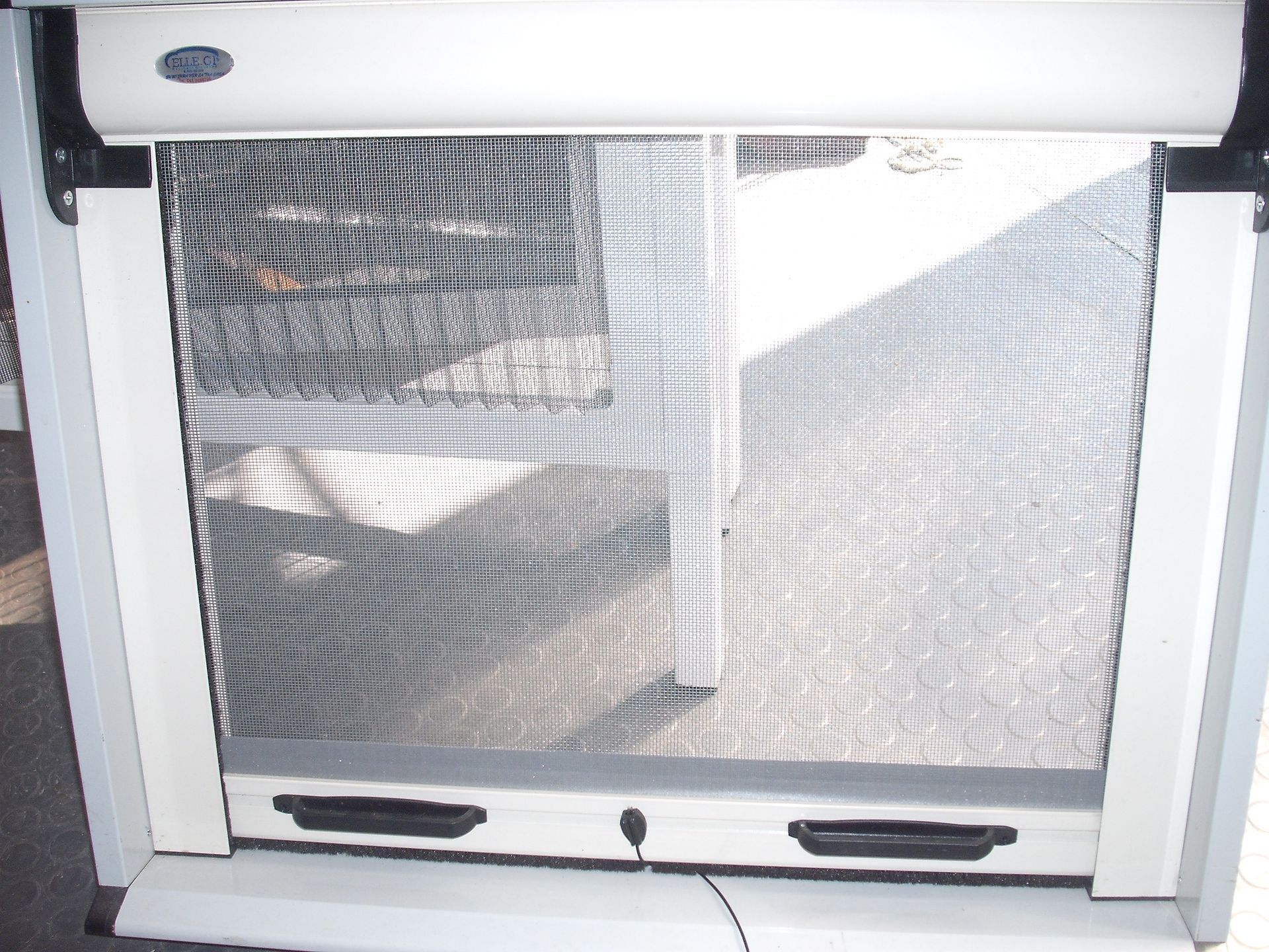 Una porta a zanzariera scorrevole bianca con maniglie nere e pannelli in rete metallica, in un ambiente interno.