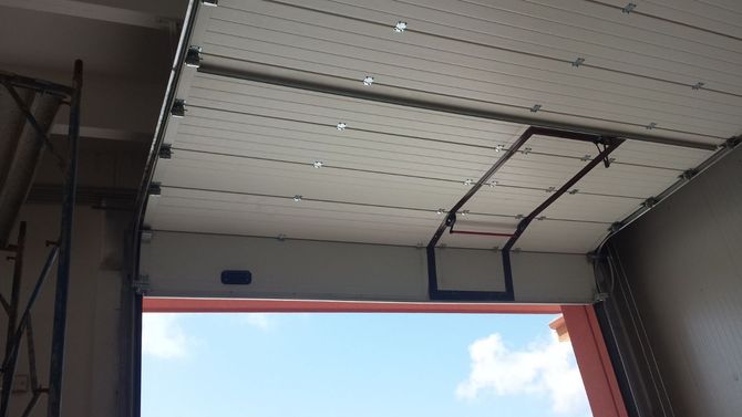 Una porta da garage sezionale bianca, parzialmente sollevata, lascia intravedere il cielo azzurro all'esterno.