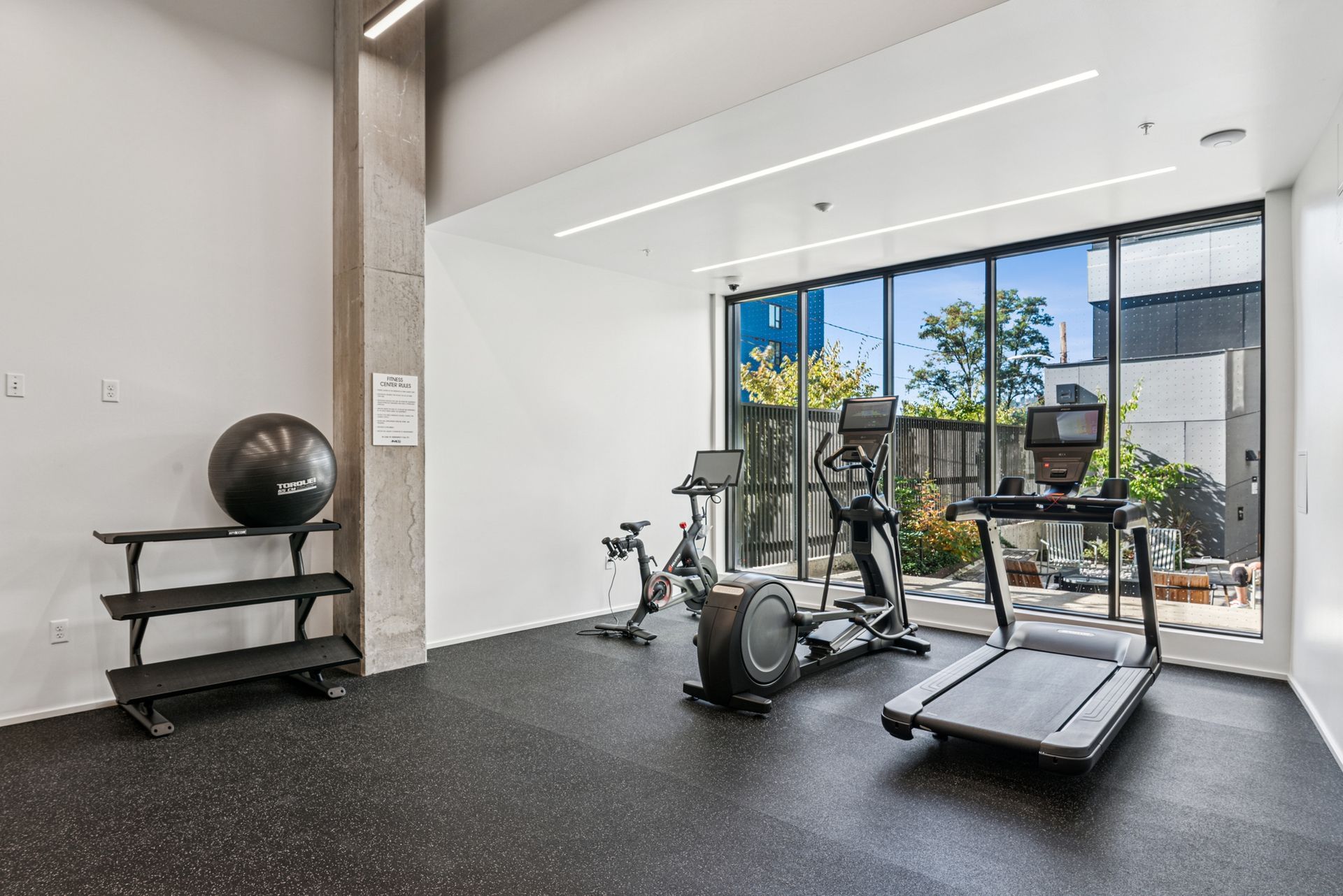 Gym interior with exercise equipment: treadmill, elliptical, stationary bike, and a shelf with a ball.