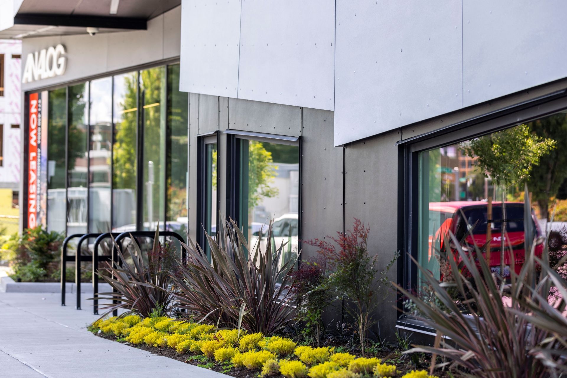 Exterior of a modern apartment building with large glass storefronts and landscaped sidewalk.