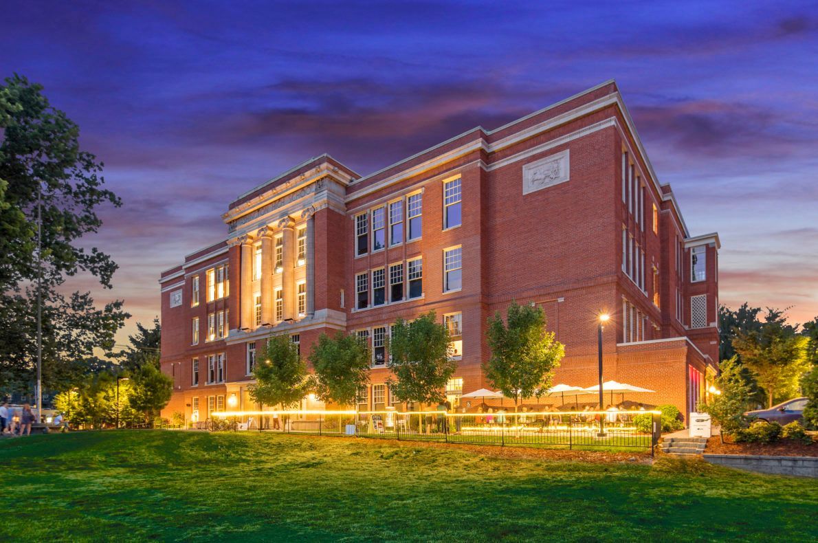 Brick building with illuminated windows and a grassy lawn at dusk.