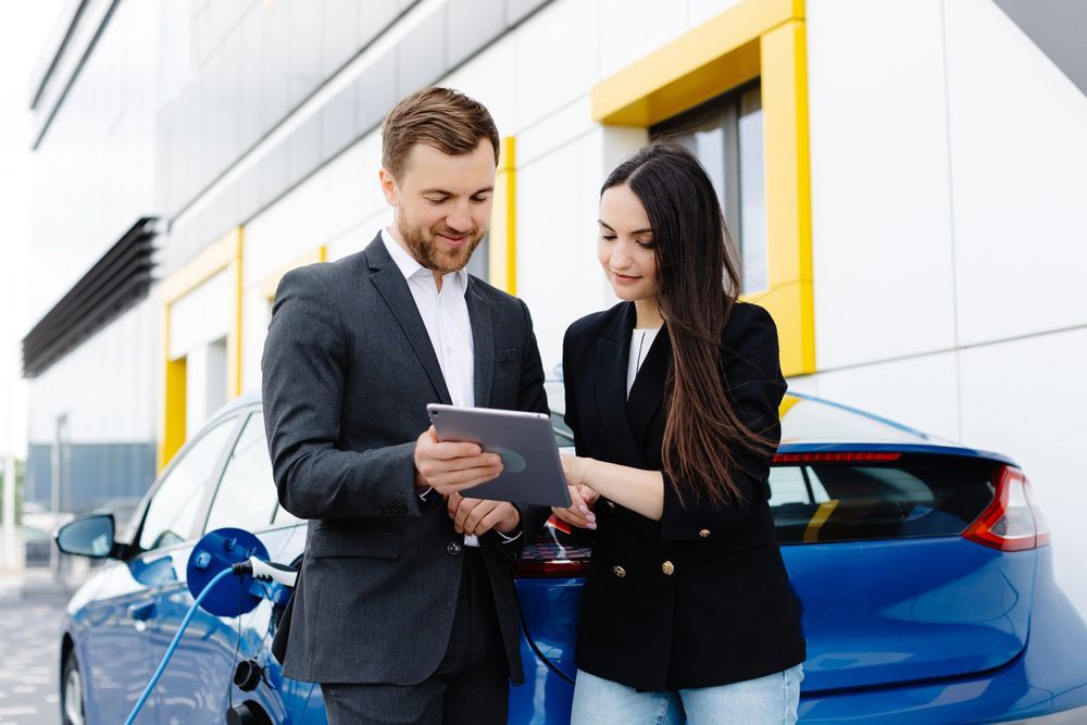 A Man and A Woman Are Looking at A Tablet in Front of An Electric Car — Start Learning Automotive in Sydney, NSW