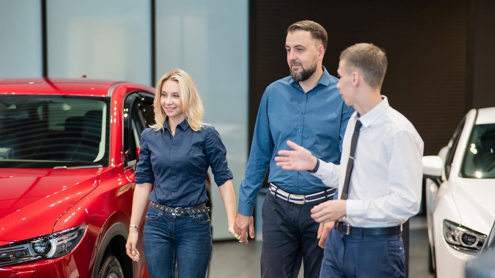 A Man and A Woman Are Standing Next to A Red Car in A Car Showroom — Start Learning Automotive in Gold Coast, QLD
