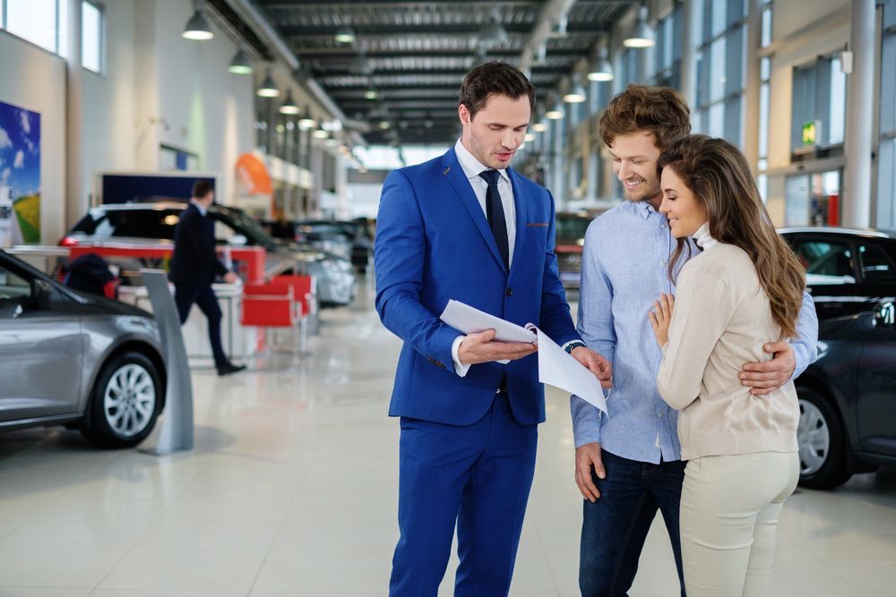 A Man in A Suit Is Talking to A Couple in A Car Showroom — Start Learning Automotive in Sunshine Coast, QLD