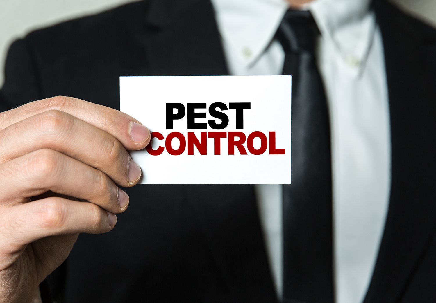 Person in suit holding a card that reads pest control.