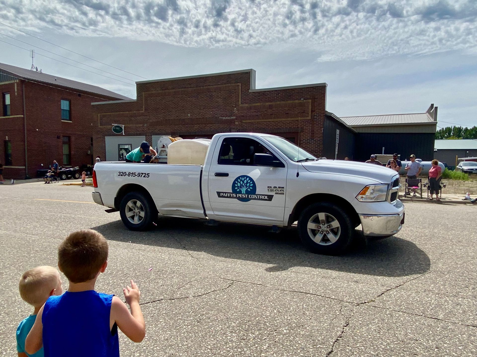 A company service truck driving through a community parade with people lining the street.