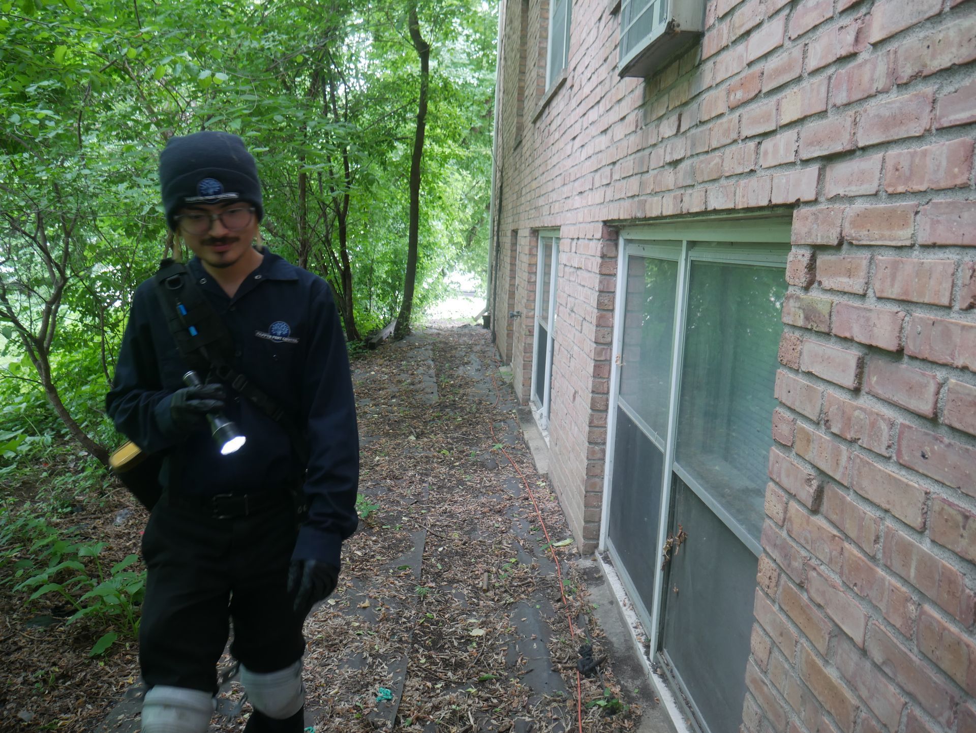 Professional pest control technician performing a perimeter inspection around a building to identify