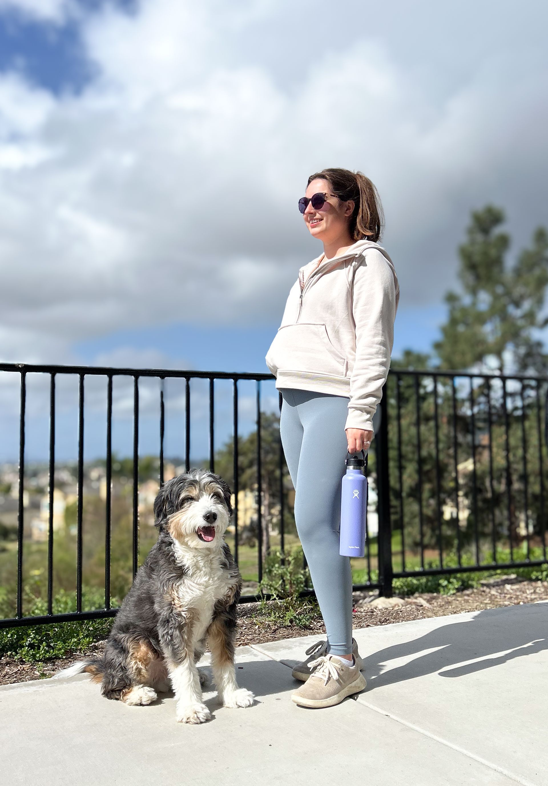 A woman is standing next to a dog on a sidewalk.