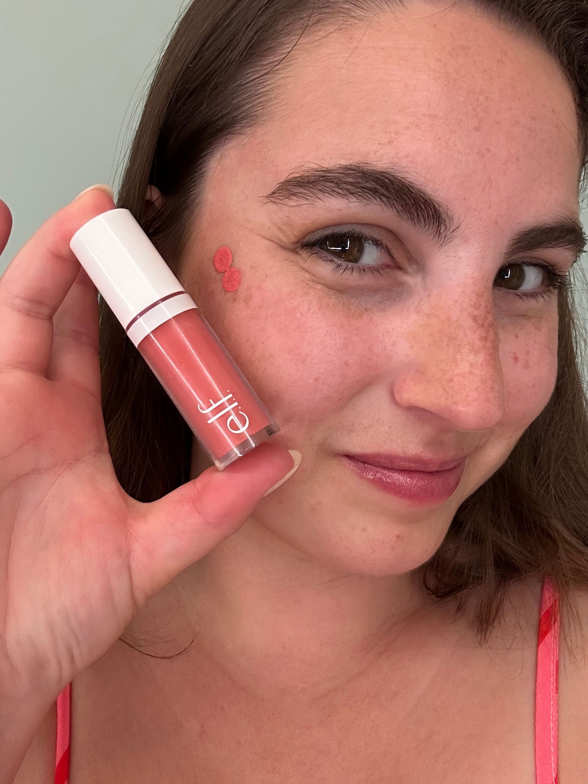 A woman is holding a bottle of liquid lipstick in front of her face.