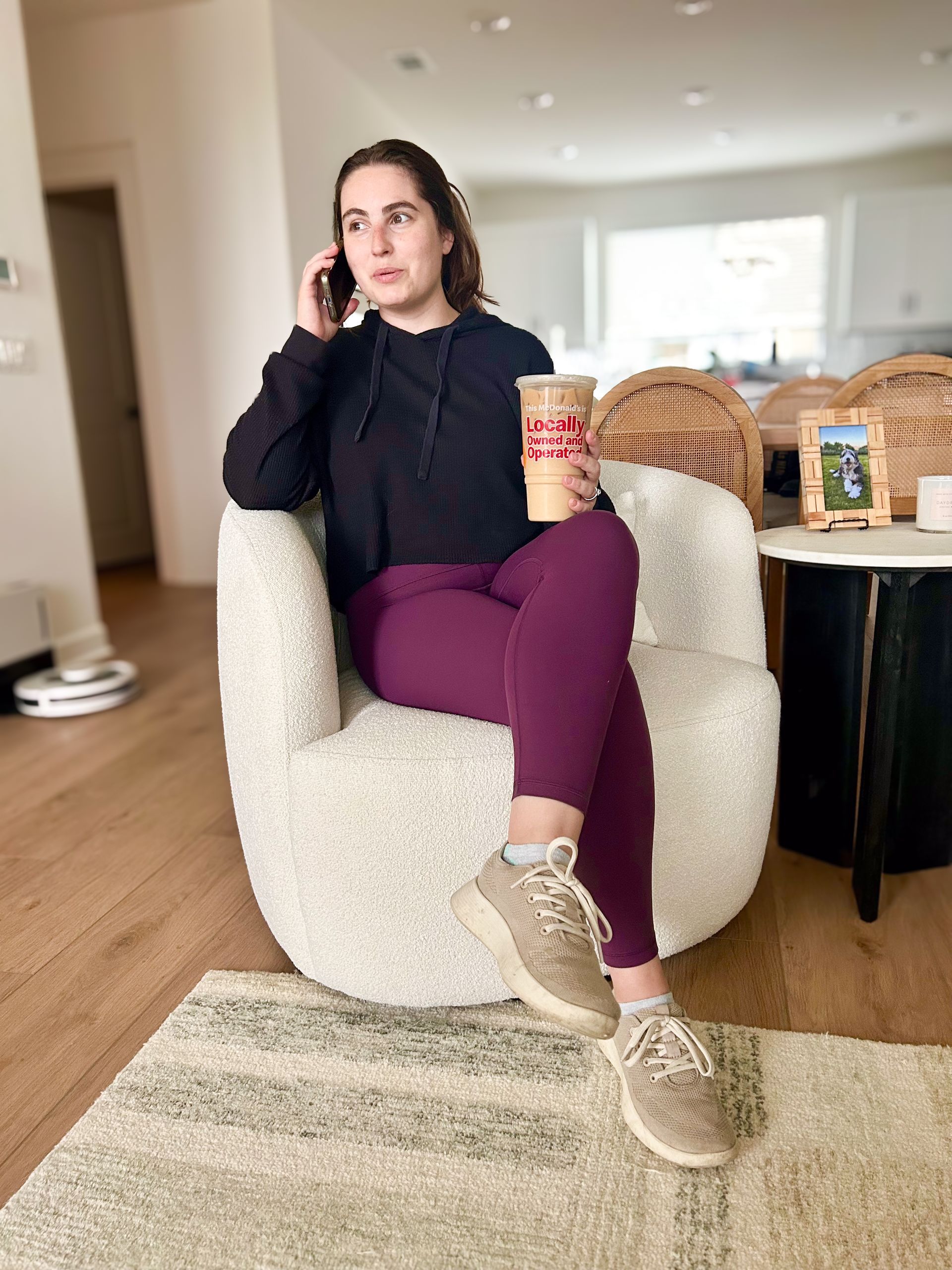 A woman is sitting in a chair talking on a cell phone while holding a cup of coffee.