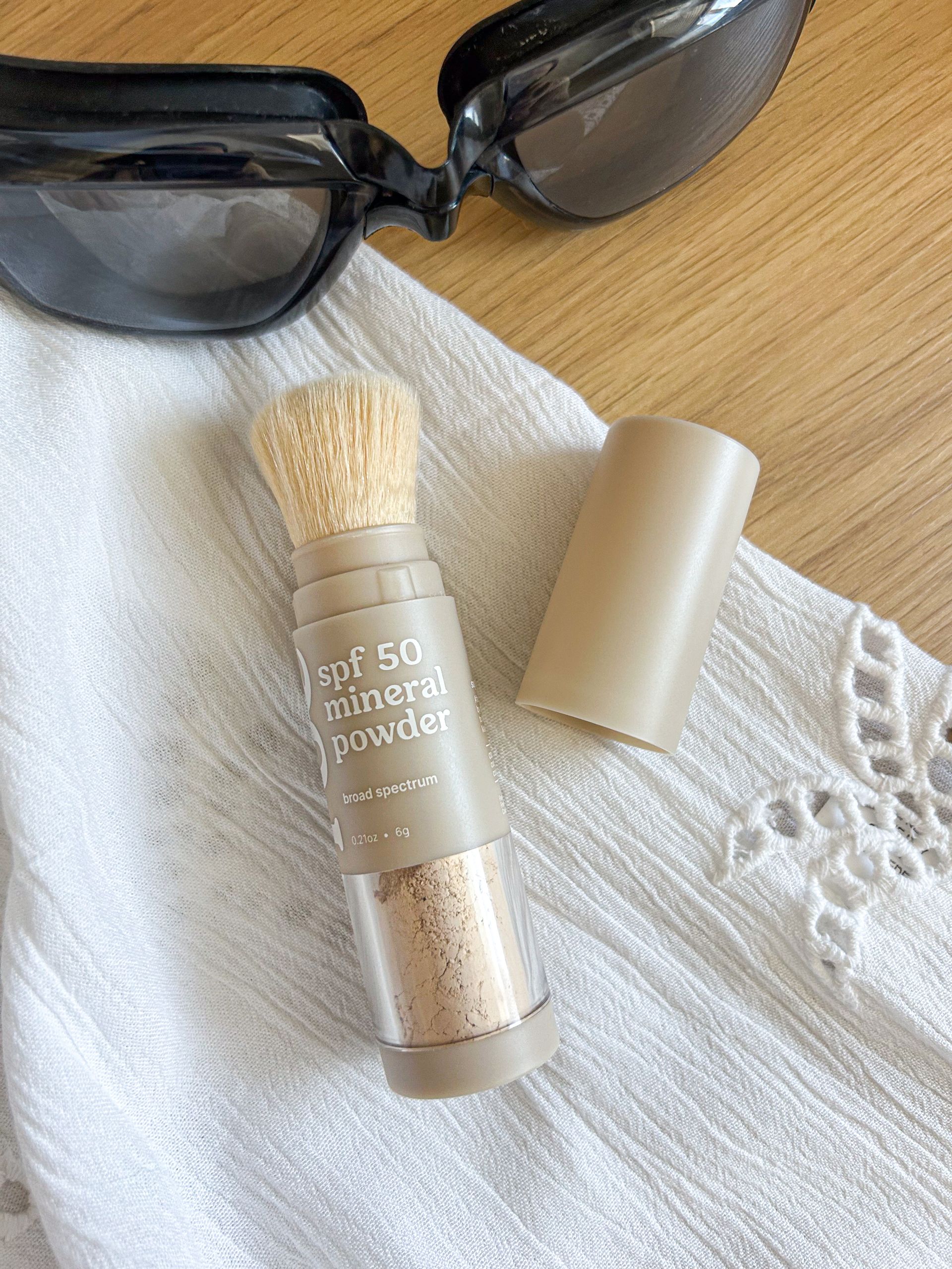 A bottle of mineral powder is sitting on a towel next to sunglasses.