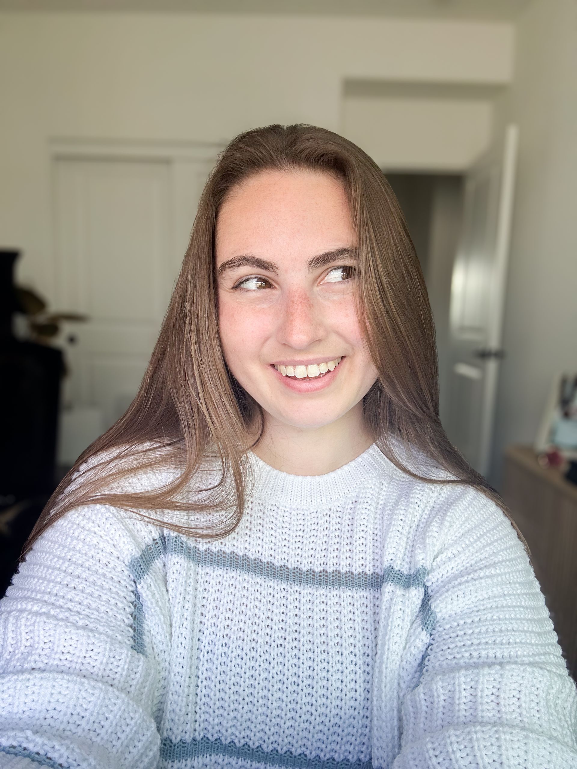 A young woman in a sweater is taking a selfie in a room.