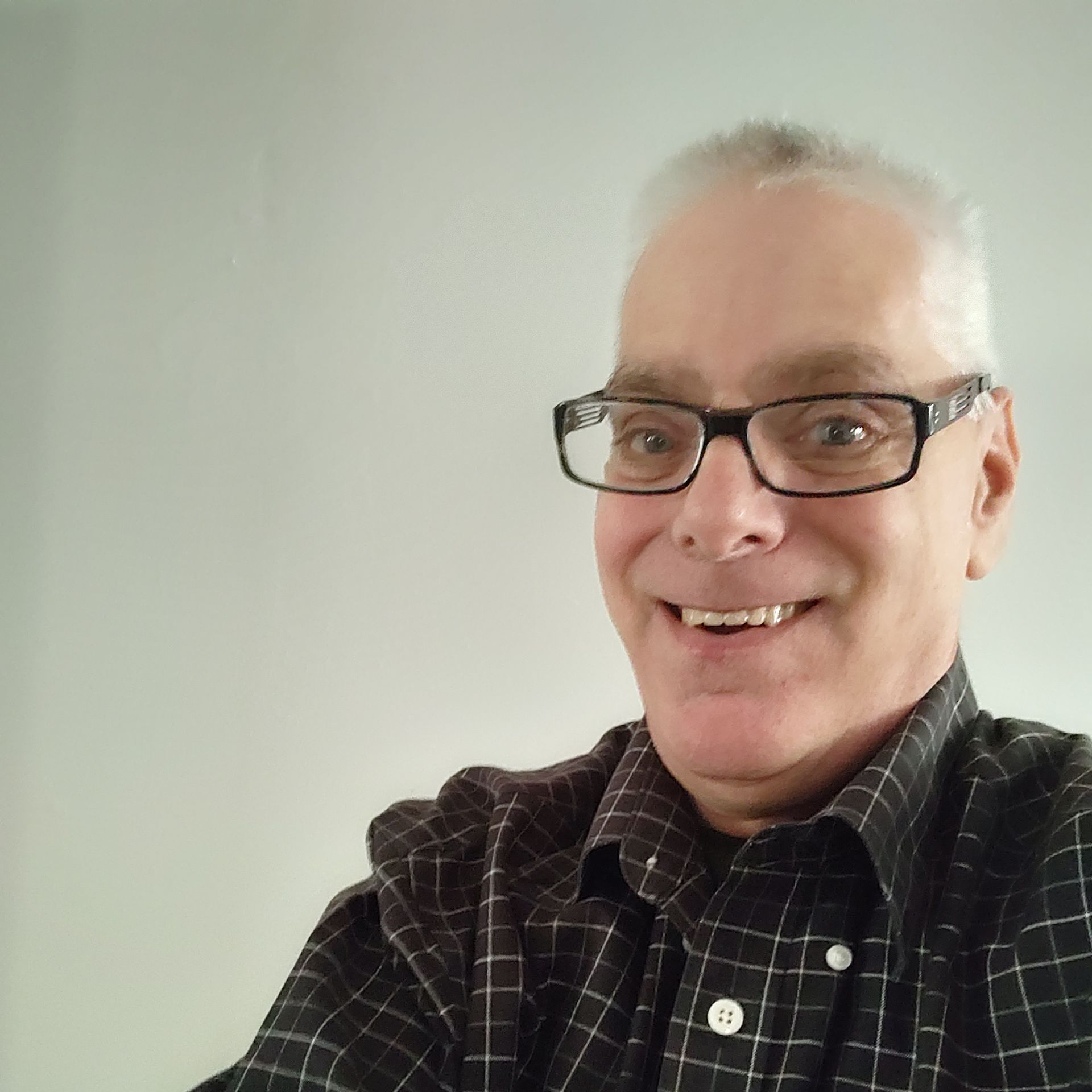 A man wearing glasses and a plaid shirt is smiling for the camera.