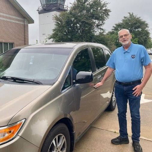 A man in a blue shirt is standing next to a car.