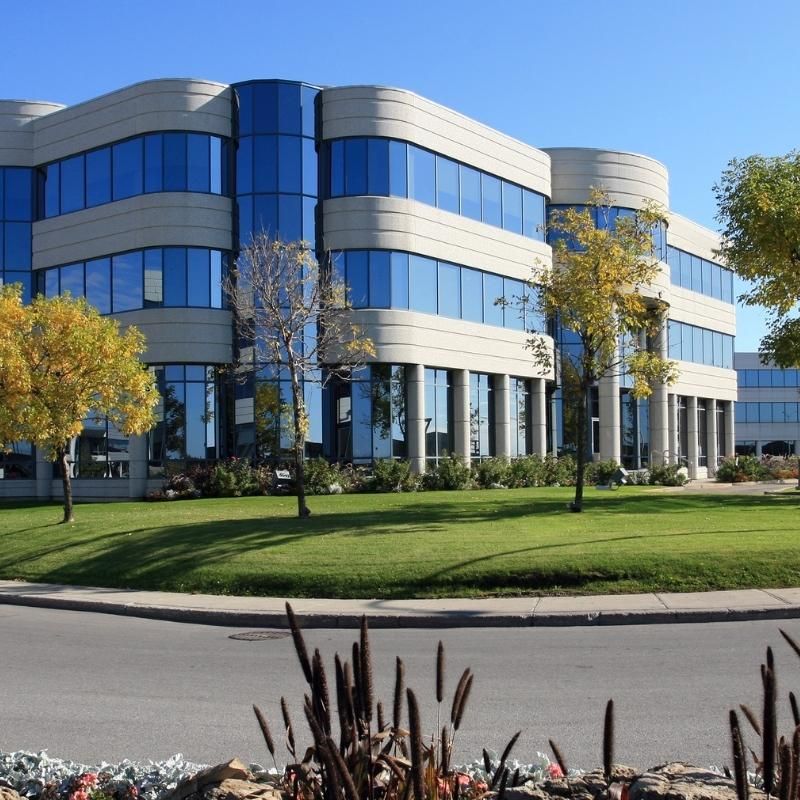 Modern, beige and blue office building with rounded corners, trees, and a green lawn.
