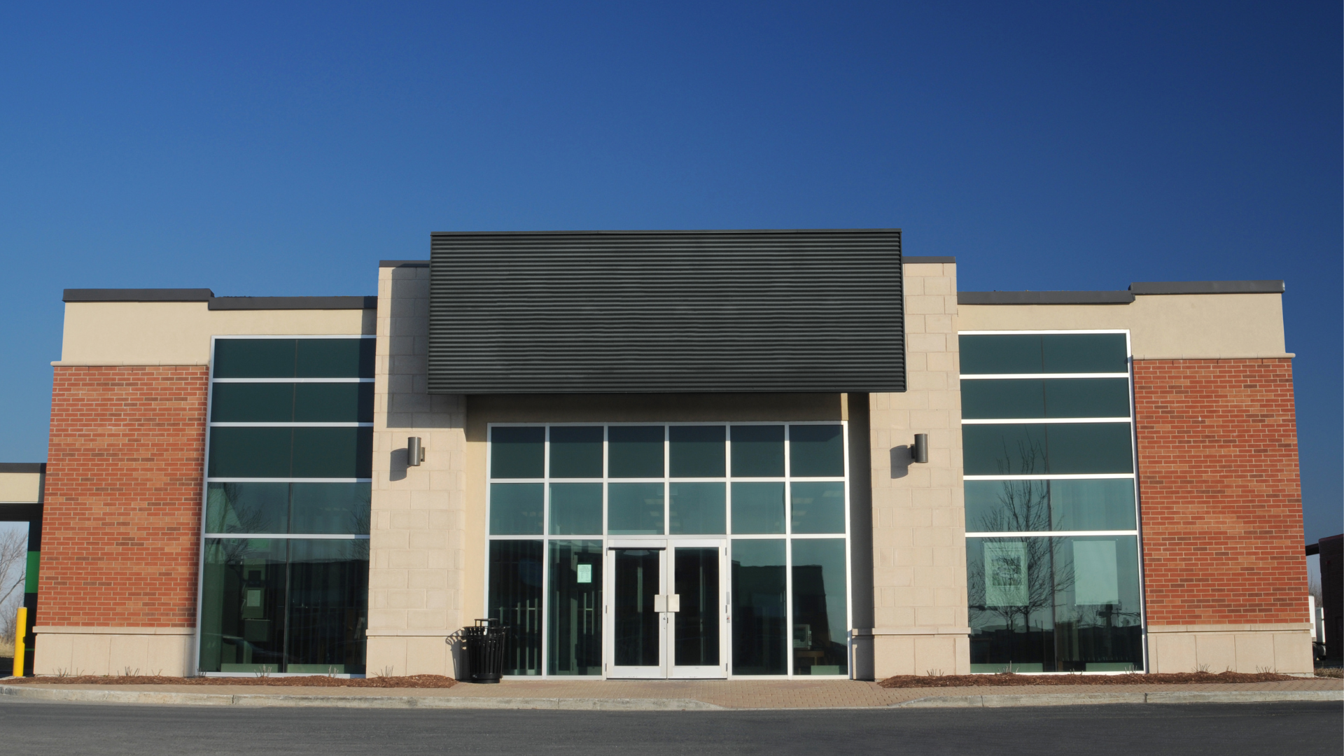Bank building with glass windows and a black awning against a clear blue sky.