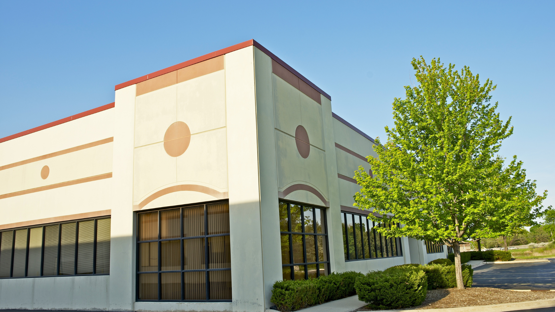 Commercial building with large windows, beige facade, and a small tree.