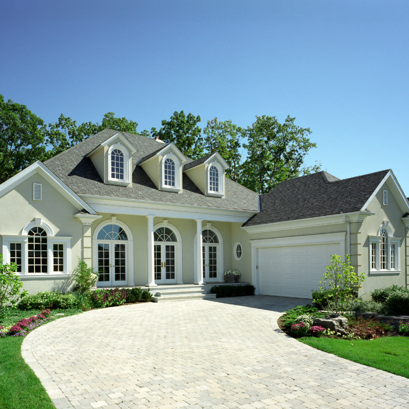 Elegant, two-story home with a long driveway, white facade, and lush landscaping under a blue sky.