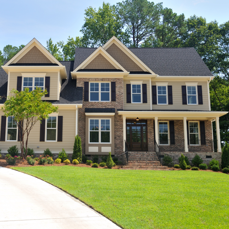 Two-story house with beige siding, brick facade, black shutters, green lawn, and a driveway.
