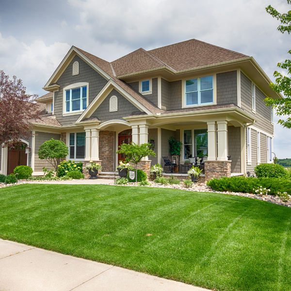 Two-story house with green siding, brown roof, beige trim, and well-manicured lawn.