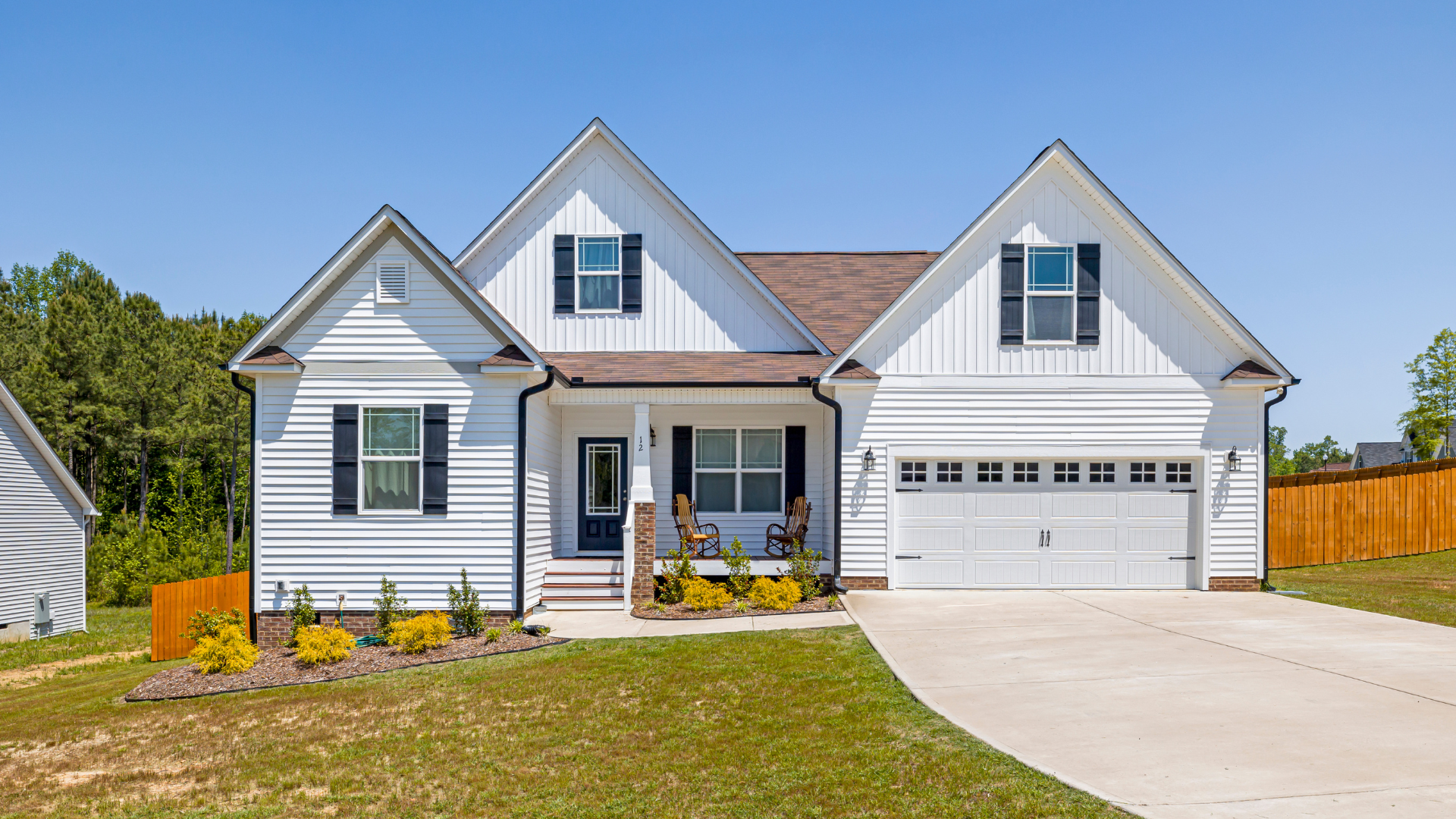 White house with black shutters and brown roof on a sunny day.