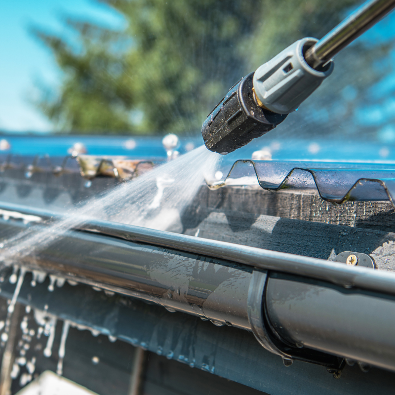 Pressure washing a dark grey gutter, spraying water.