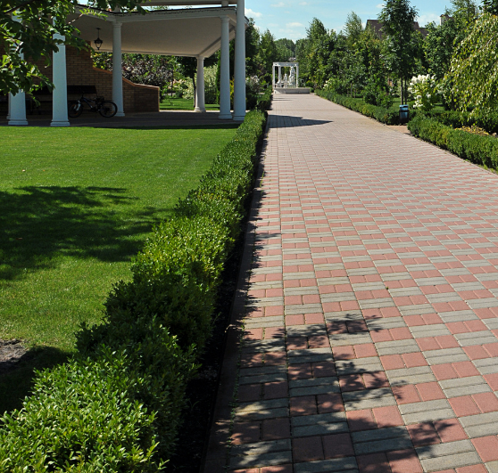 Brick walkway lined with hedges, leading to a gazebo and garden with a blue sky.