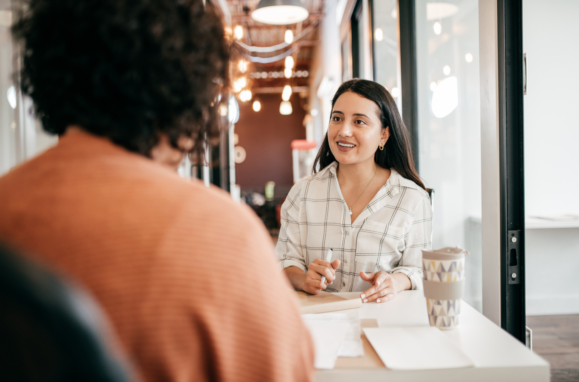 Woman smiling and talking with a colleague at a table in a modern office.