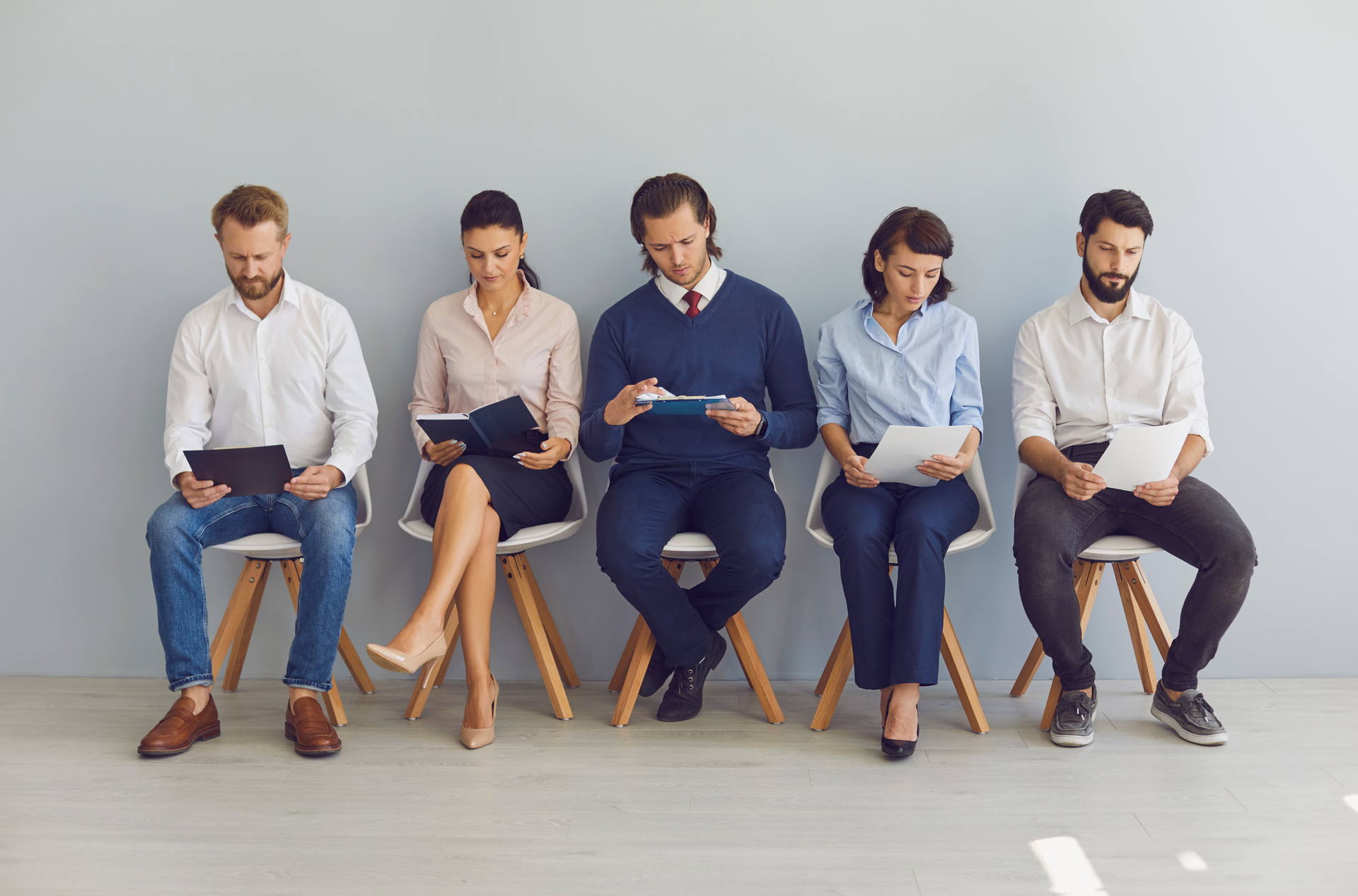 Five people seated in a row, waiting in for interview while reading resumes