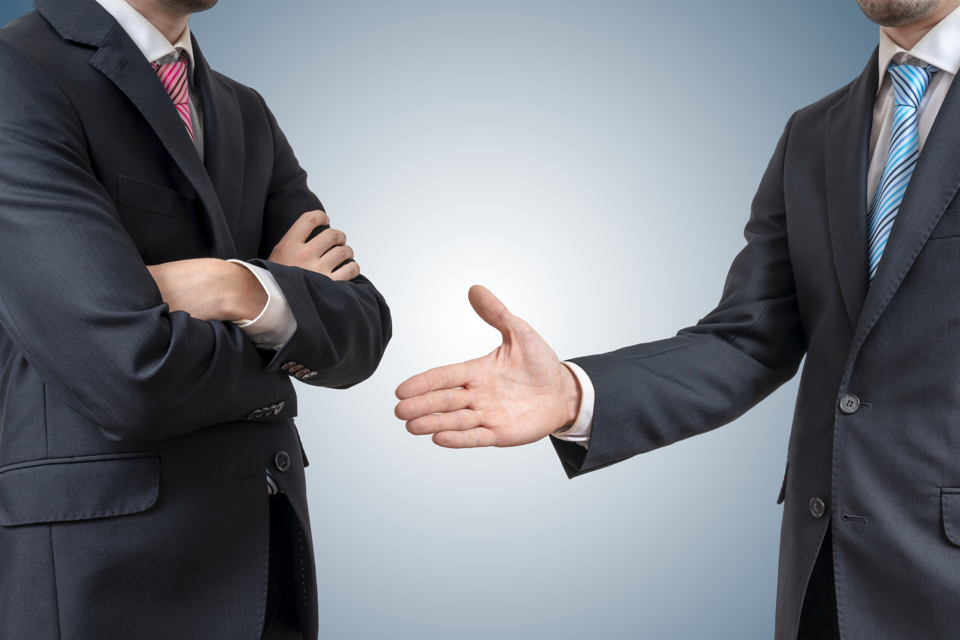 Two men in suits, one crossing arms while the other extends a hand for a handshake. 