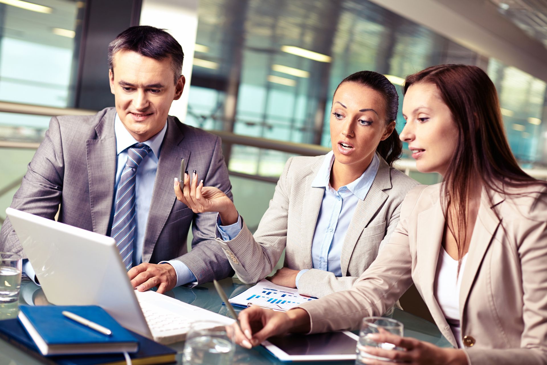 Three business professionals in suits are engaged in a meeting, focused on a laptop screen.