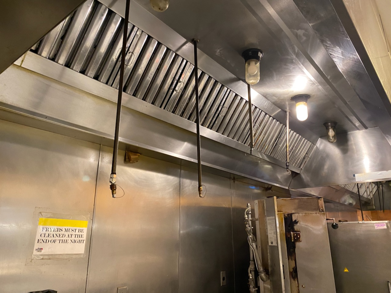 Stainless steel kitchen exhaust hood with sprinklers and lights.