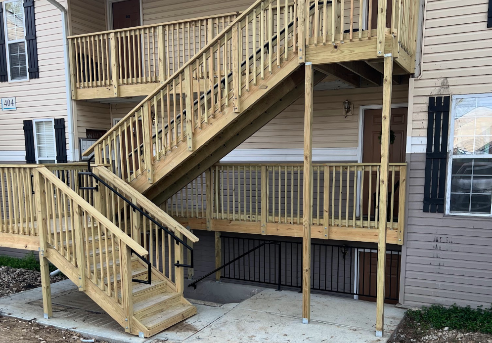 A wooden deck with stairs leading up to the second floor of a building.