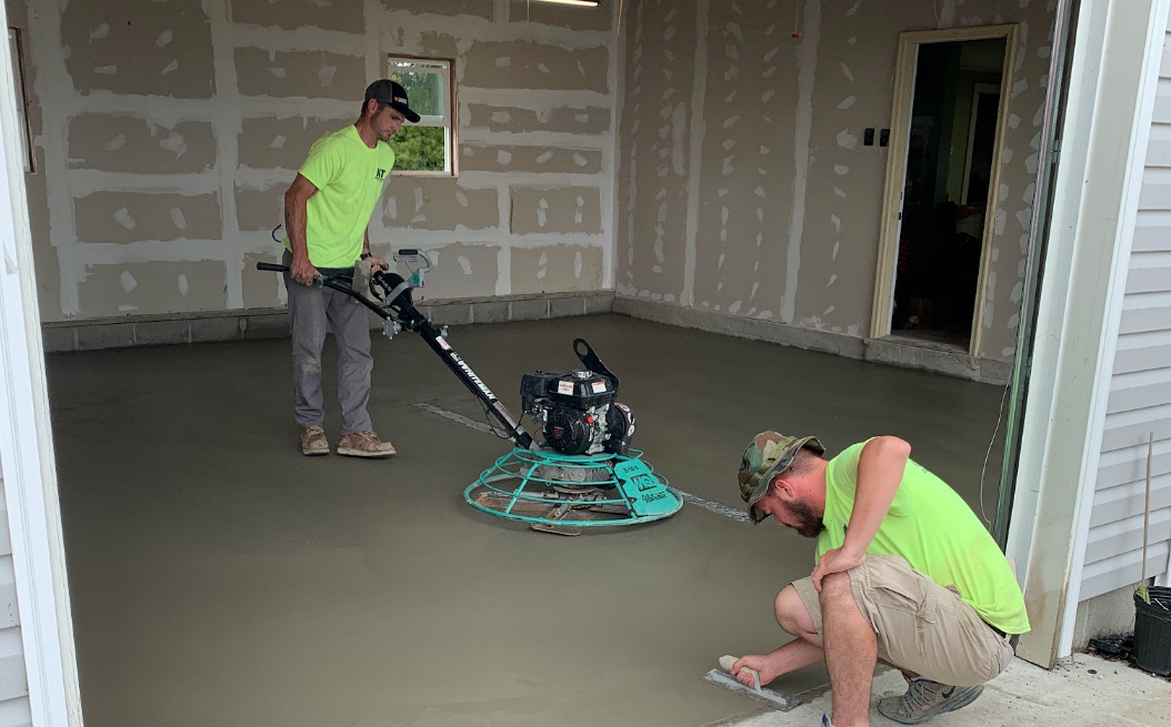 Two men are working on a concrete floor in a garage.