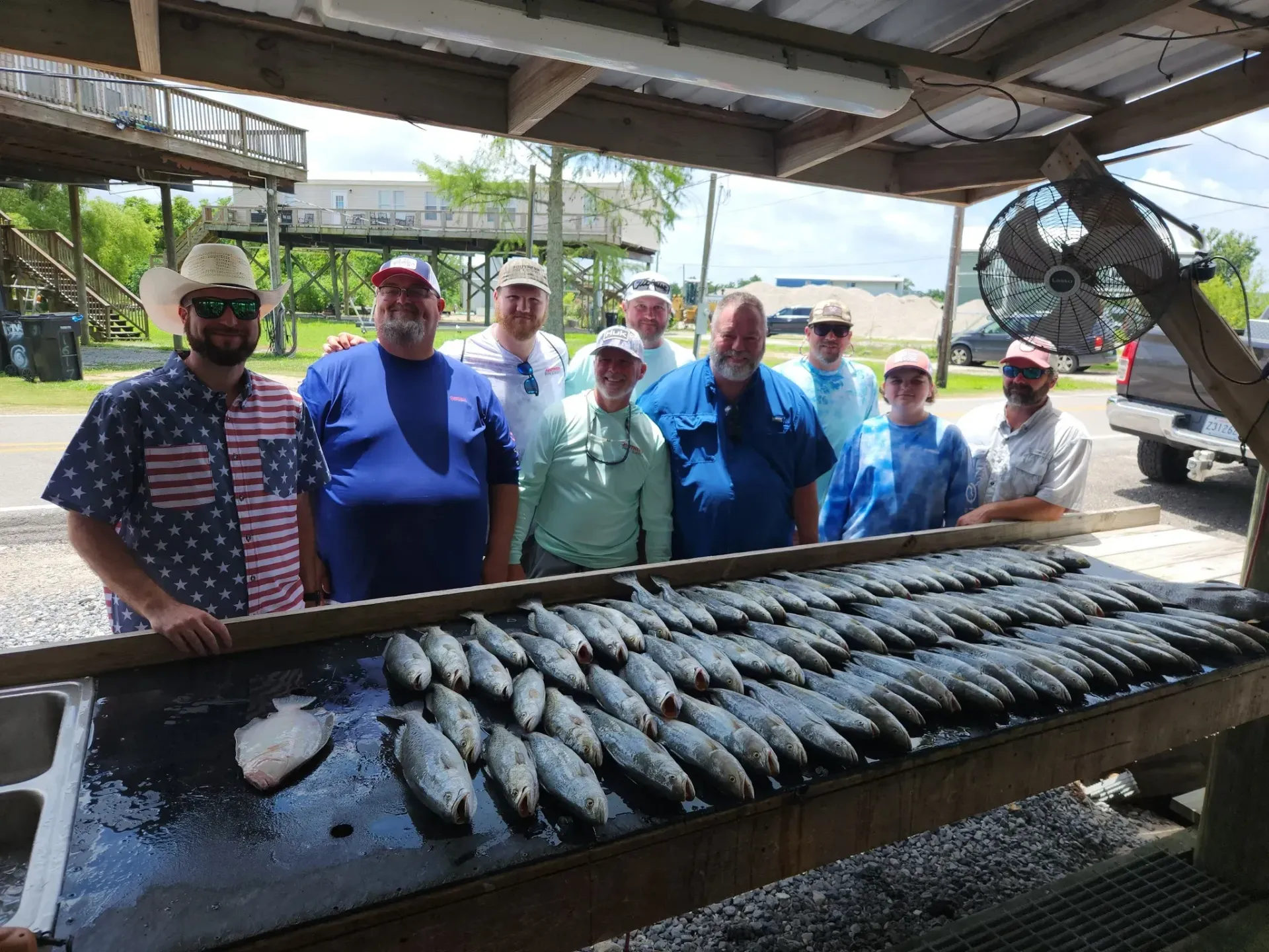 A group of people standing behind a wooden table filled with fresh fish at an outdoor cleaning station.