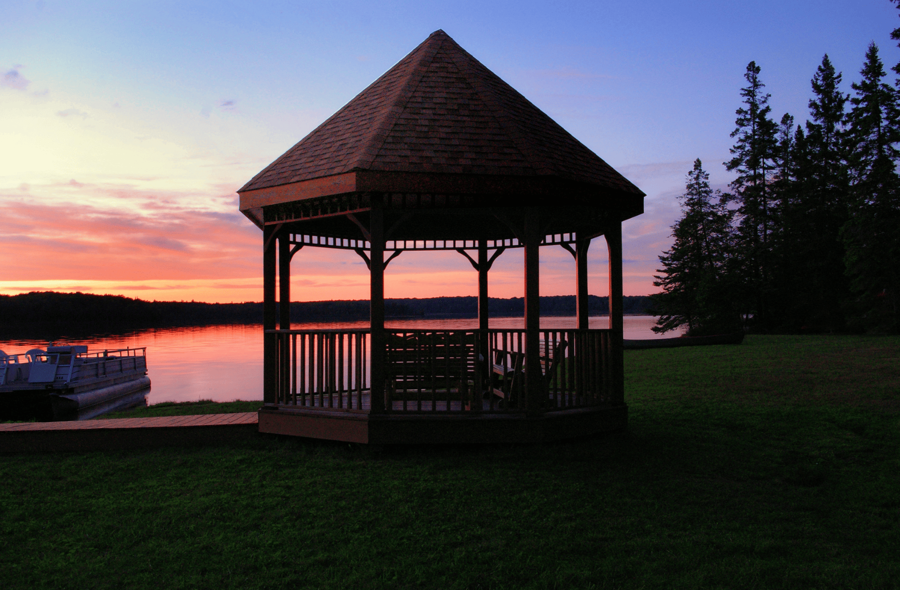 A gazebo sits on the shore of a lake at sunset