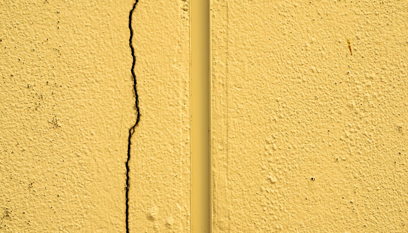 Yellow stucco wall with a vertical crack on the left and a vertical strip on the right.