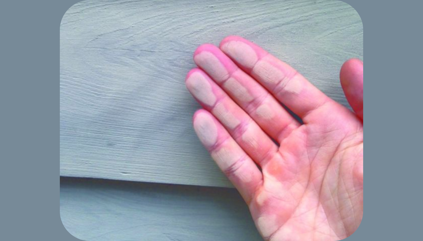 Hand with pale paint residue on fingertips, touching light-colored wooden surface.