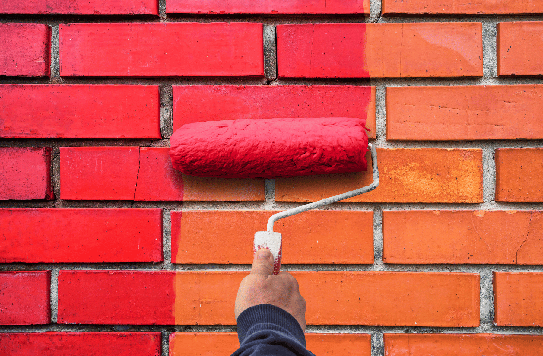 A person is painting a brick wall red with a roller.