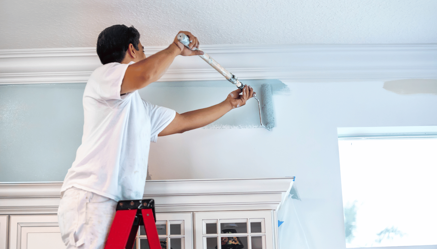 A man is standing on a ladder painting a wall.