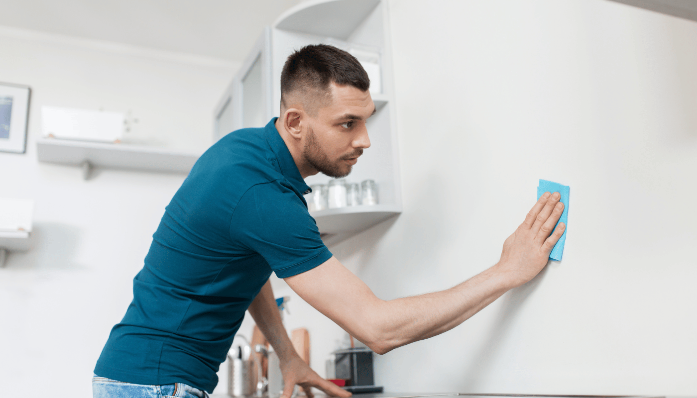 A man is cleaning a wall with a cloth in a kitchen.