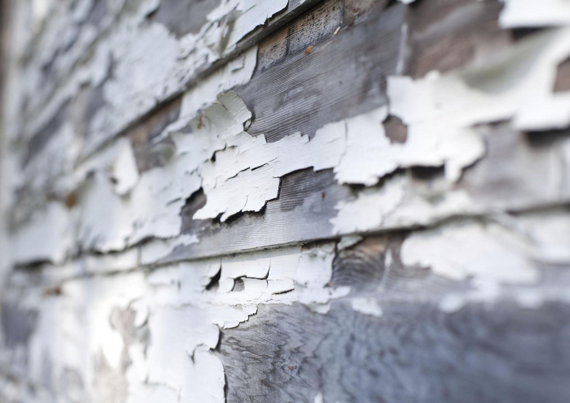 Peeling white paint on weathered wooden siding.