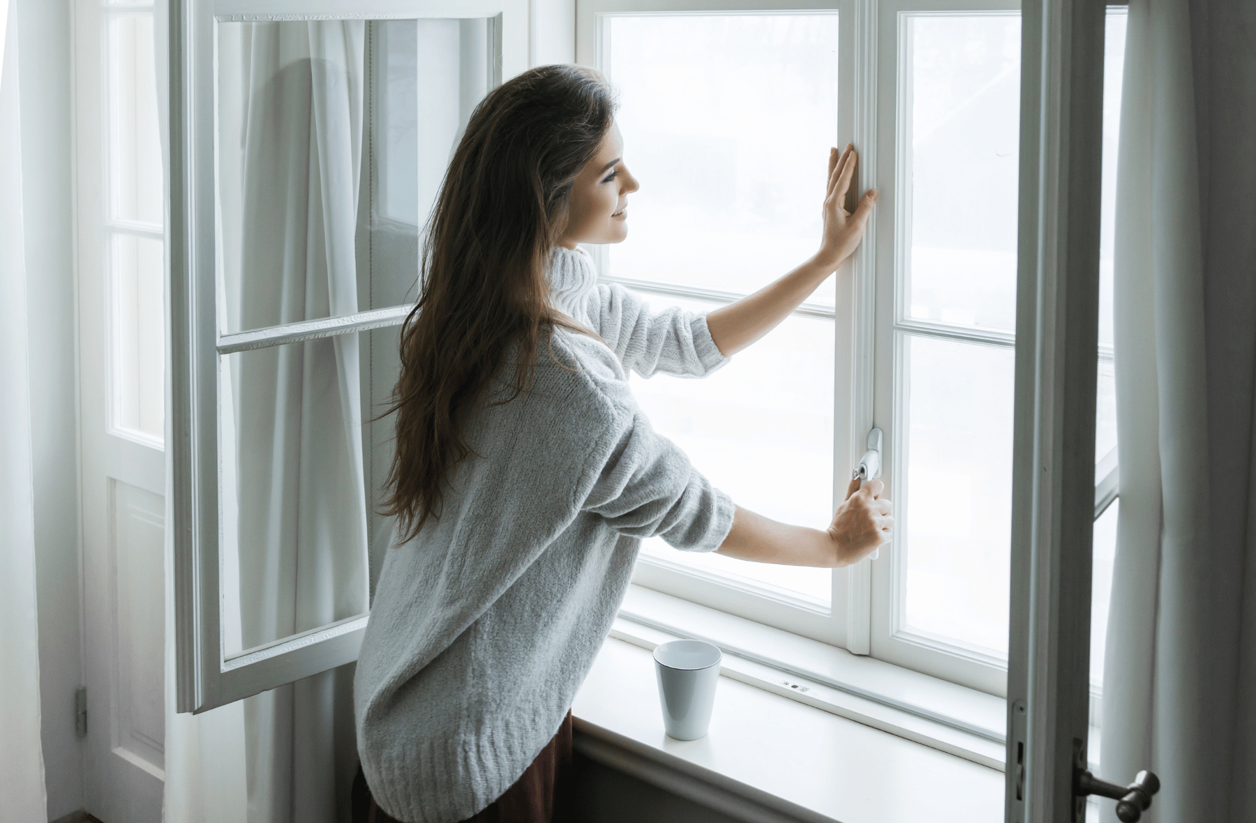 A woman is standing on a window sill looking out the window.