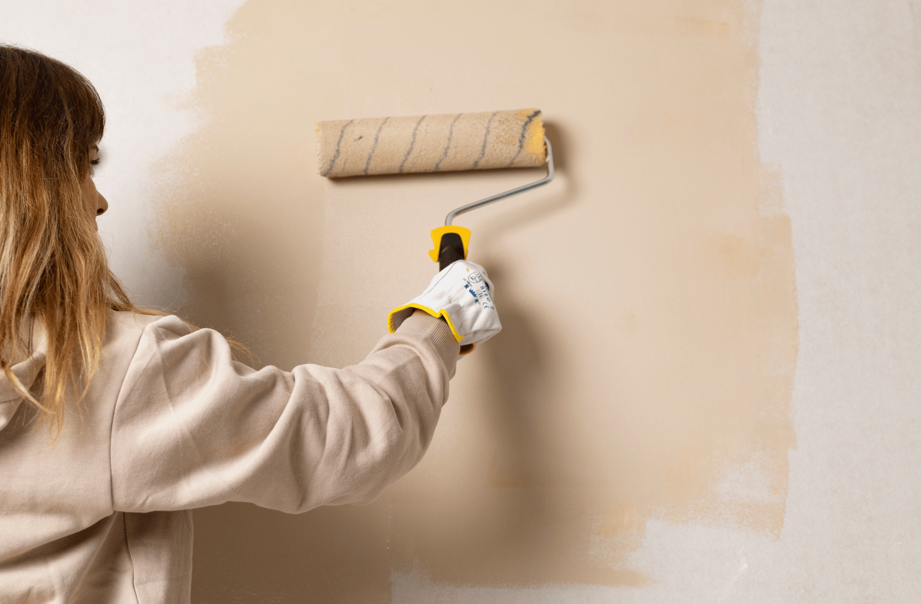 A woman is painting a wall with a paint roller.