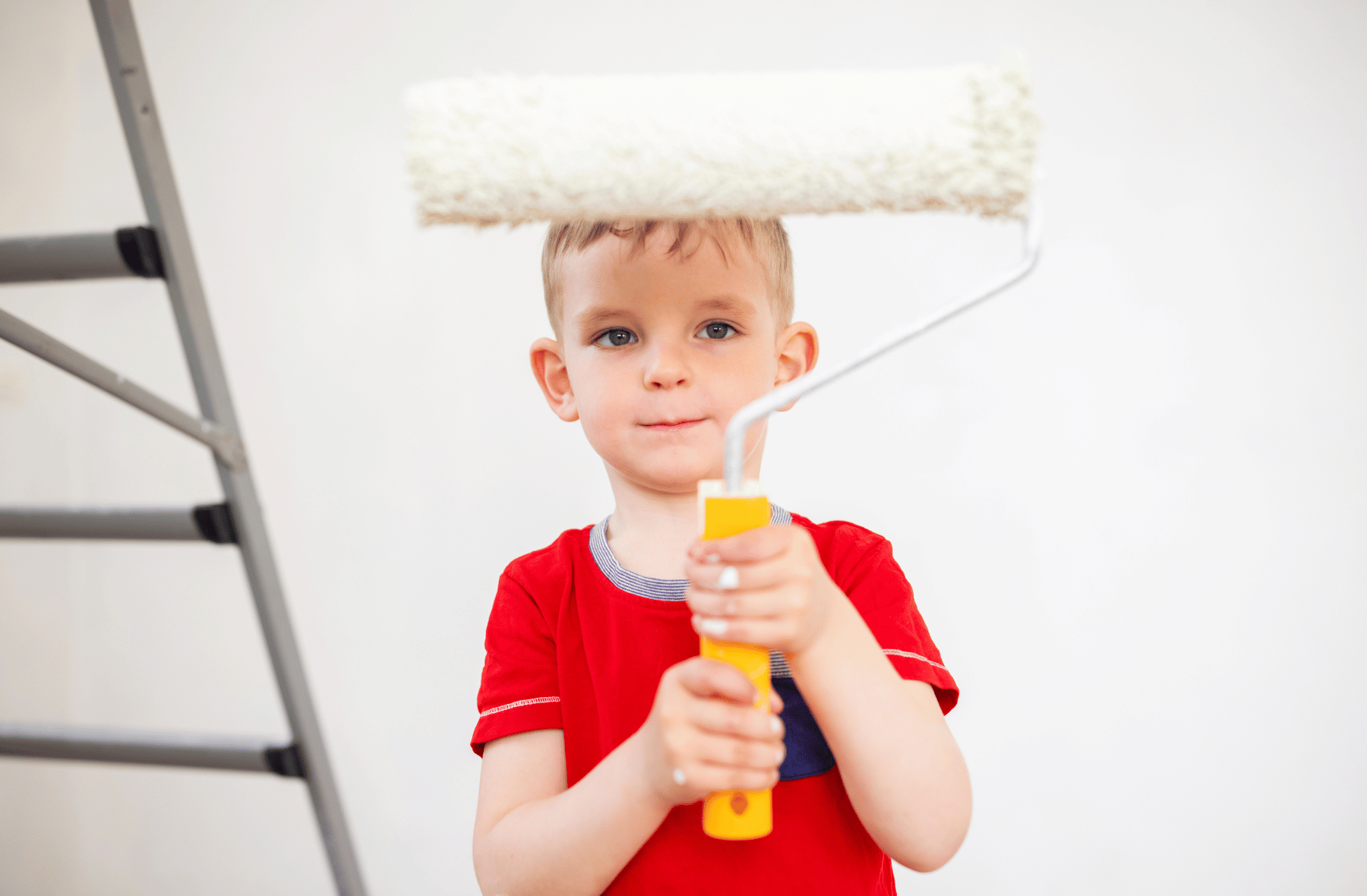 A young boy is holding a paint roller on his head.