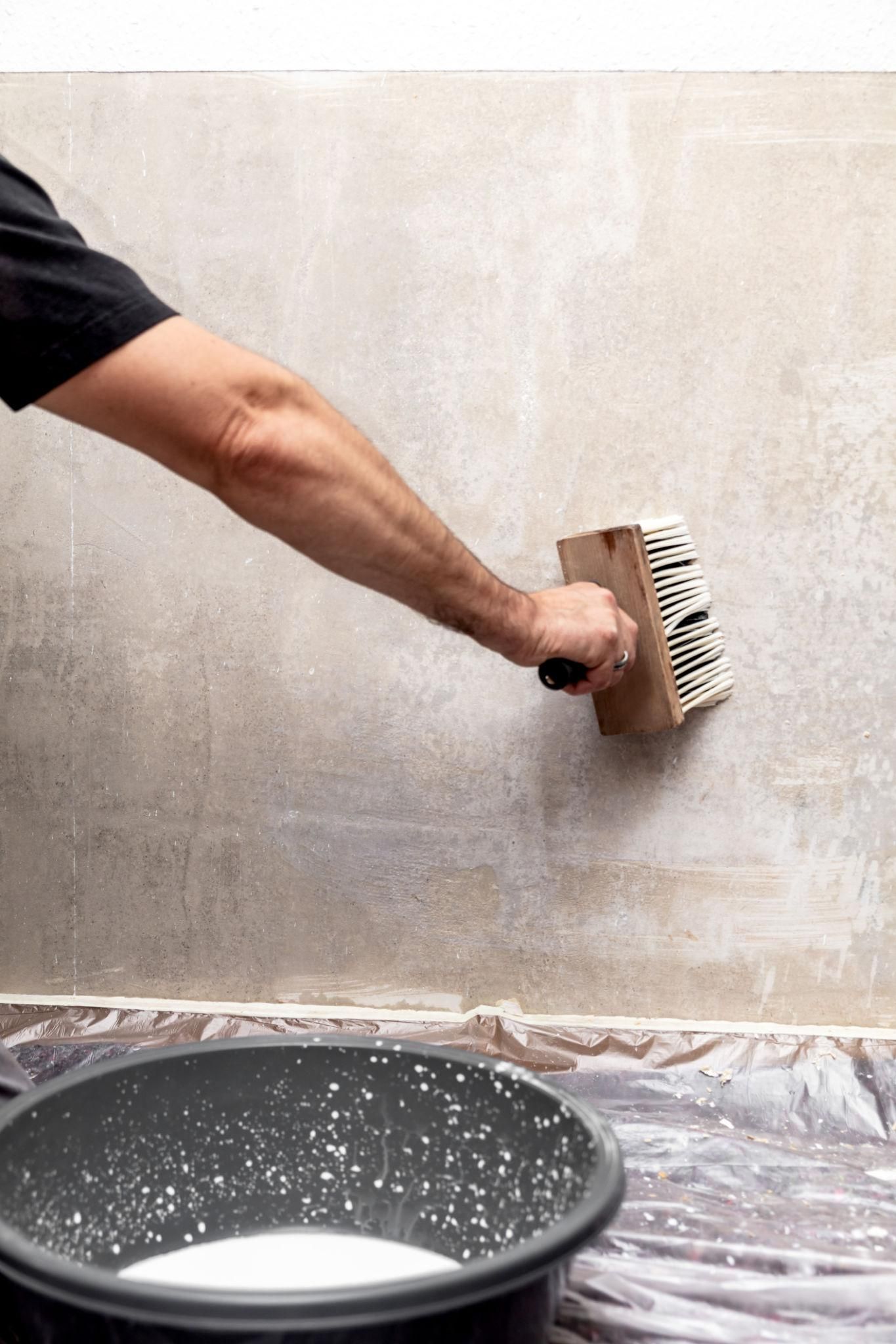 applying wallpaper glue to a wall with a brush